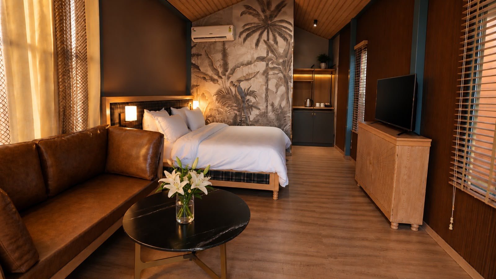 A cottage interior with a made bed, leather sofa, painted palm mural and a tea and coffee station