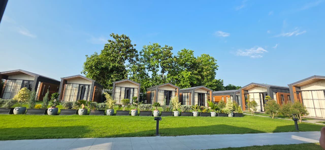 A row of independent cottages at Aanandam by Saryu overlooking a manicured lawn under a clear blue sky