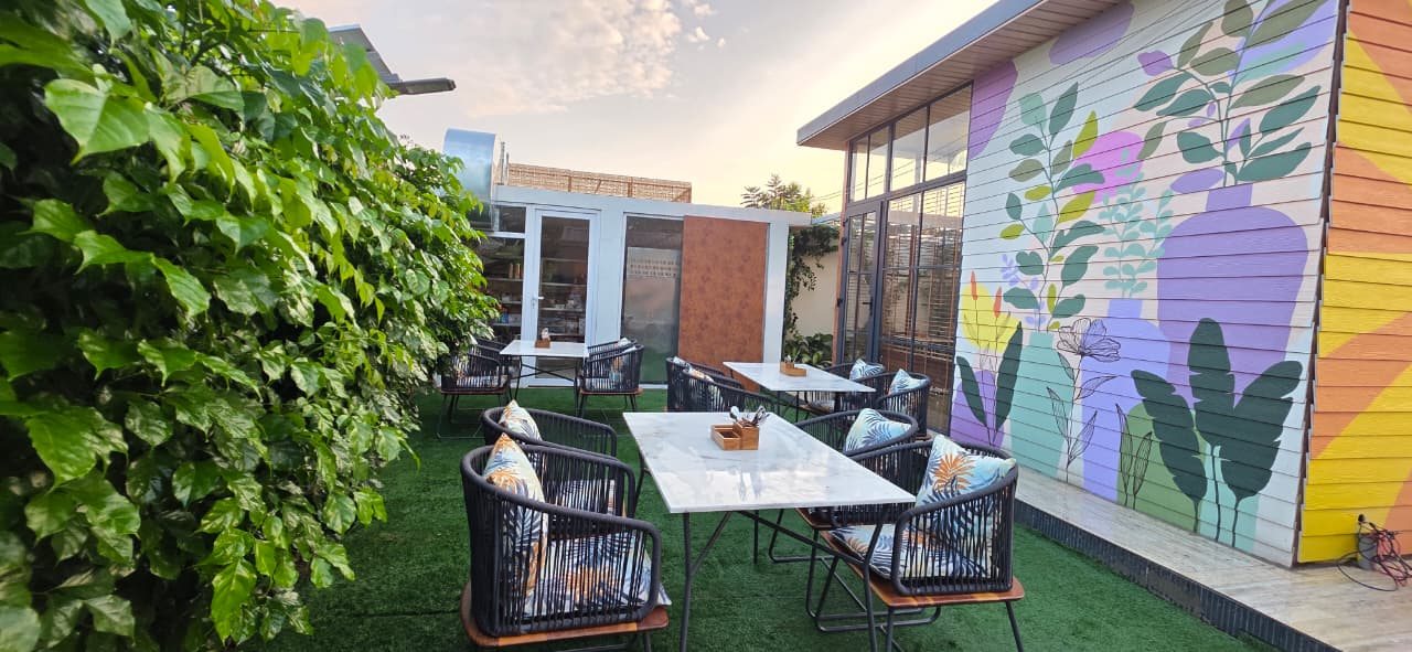 Outdoor garden dining area at Aanandam with marble tables, woven chairs and a painted botanical mural